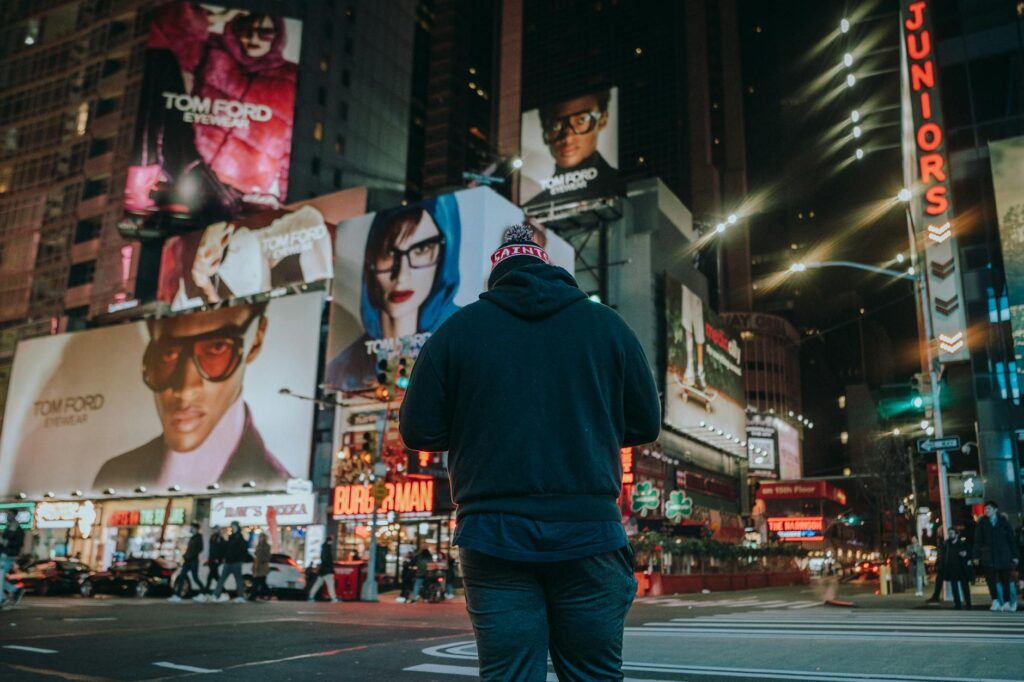 man standing on street with advertisements on buildings at night